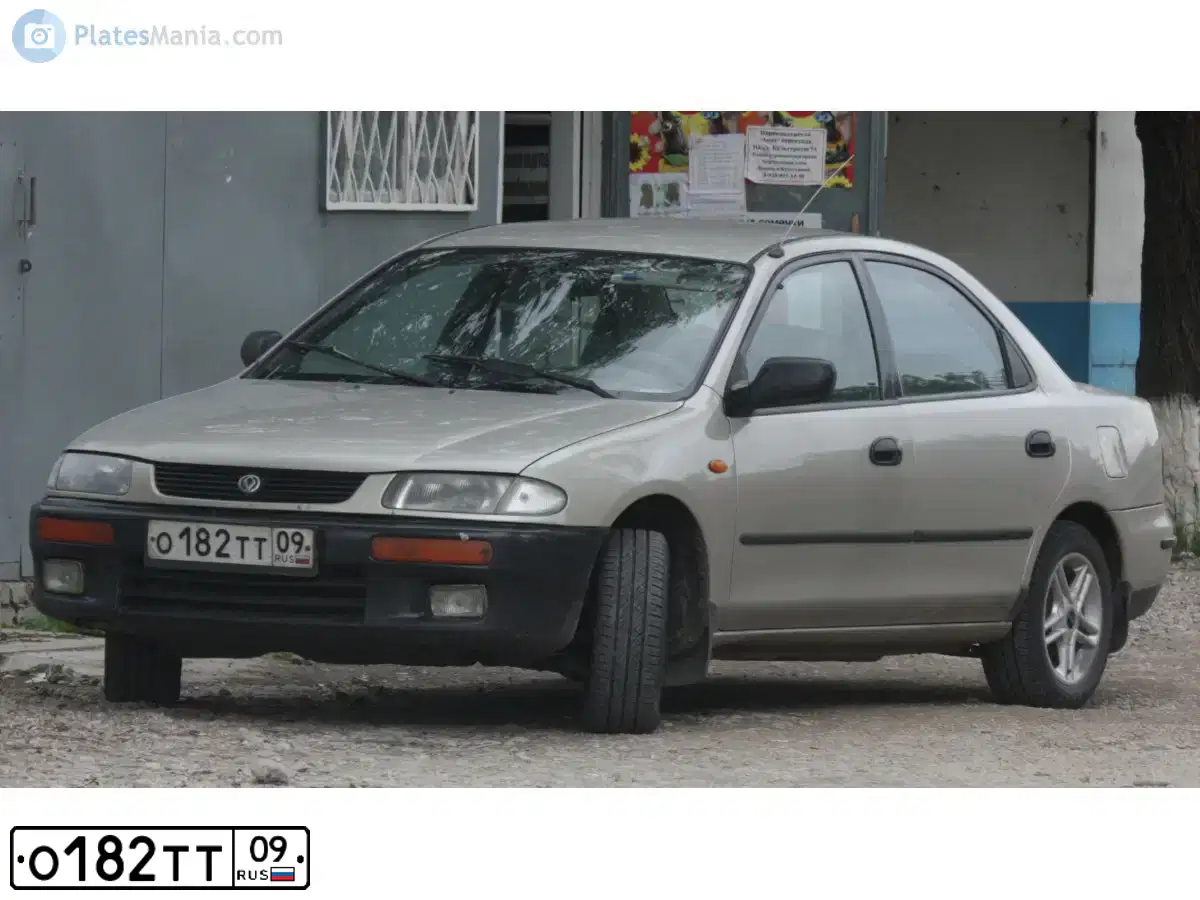 Фото автомобиля MAZDA 323, 1996 — госномер О182ТТ09. Цвет: СВЕТЛО-СЕРЫЙ