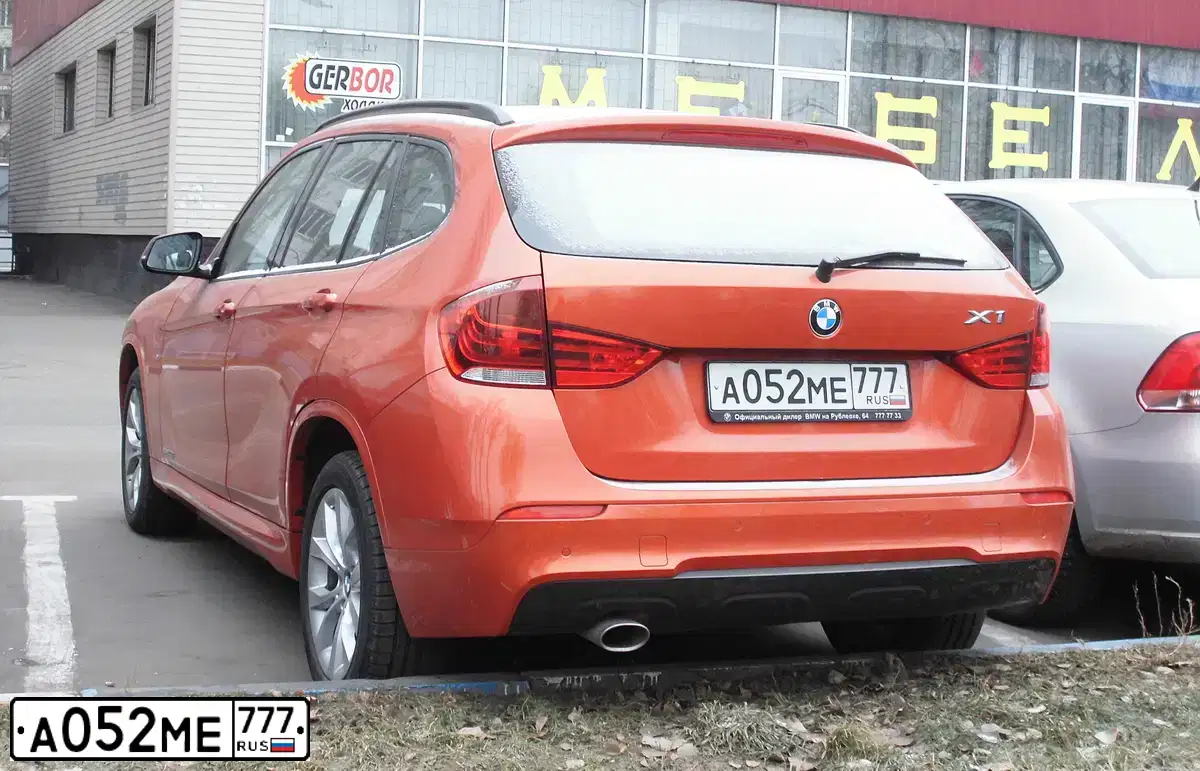 Фото автомобиля BMW X1, 2014 — госномер А052МЕ777. Цвет: ОРАНЖЕВЫЙ